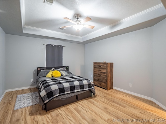 bedroom with visible vents, a raised ceiling, baseboards, and wood finished floors