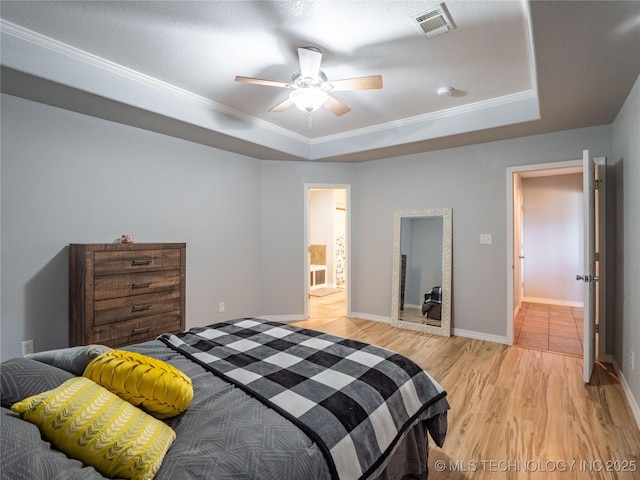 bedroom with a tray ceiling, baseboards, visible vents, and light wood finished floors