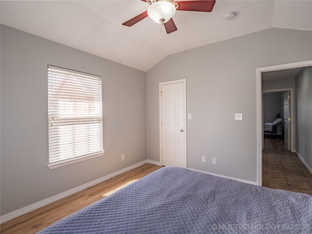 bedroom with wood finished floors, a ceiling fan, baseboards, and vaulted ceiling