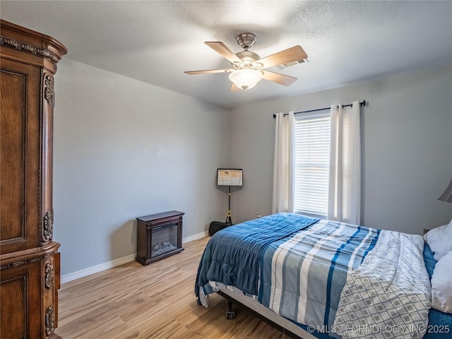 bedroom featuring ceiling fan, light wood-style floors, baseboards, and a textured ceiling