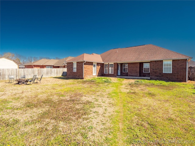 back of house with brick siding, a yard, a fire pit, and a fenced backyard