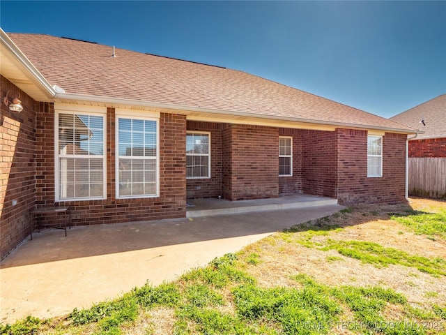 rear view of house featuring fence, brick siding, a shingled roof, and a patio area