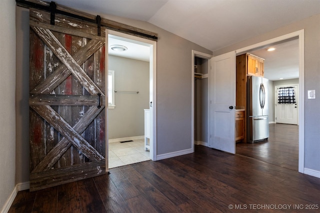 interior space featuring vaulted ceiling, a barn door, dark wood finished floors, and baseboards