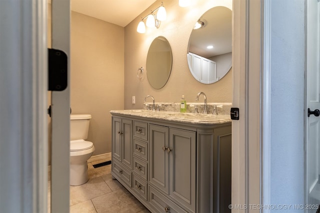 bathroom with double vanity, a sink, toilet, and tile patterned floors