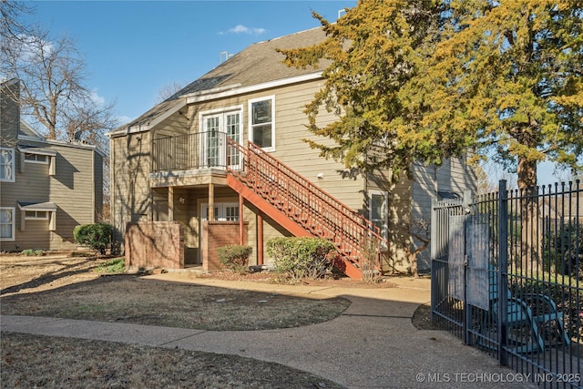 view of front of home featuring french doors, brick siding, fence, and stairway