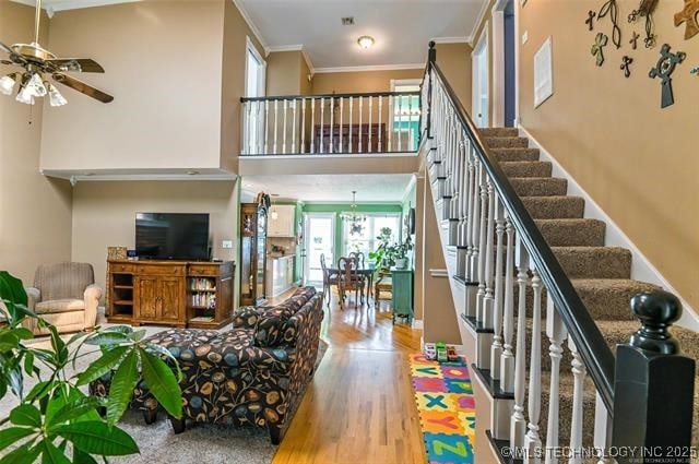 interior space with crown molding, a towering ceiling, a ceiling fan, wood finished floors, and stairs