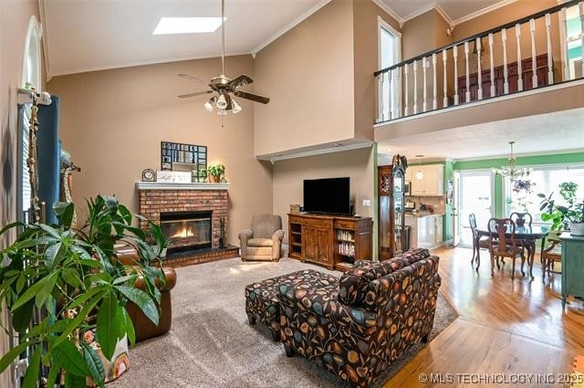 living room with ceiling fan with notable chandelier, ornamental molding, a fireplace, and a high ceiling