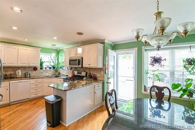 kitchen featuring appliances with stainless steel finishes, a sink, a peninsula, and light wood-style flooring