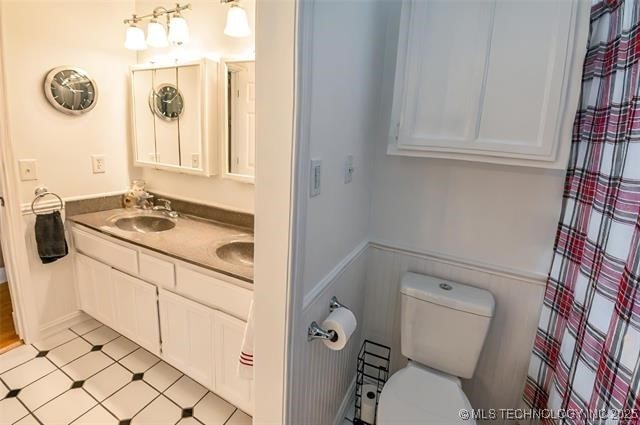 full bath with toilet, a shower with curtain, double vanity, and a sink