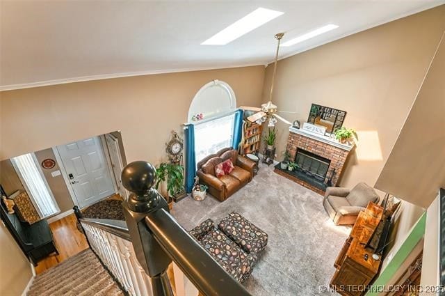 living room featuring ceiling fan, vaulted ceiling with skylight, a brick fireplace, and wood finished floors