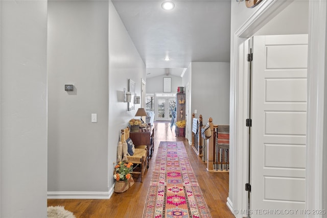 hall featuring lofted ceiling, baseboards, and wood finished floors