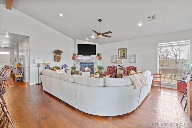 living room with lofted ceiling, recessed lighting, visible vents, a stone fireplace, and hardwood / wood-style flooring