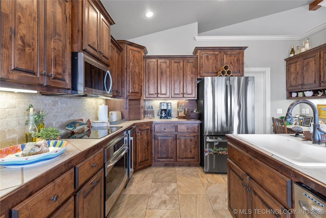 kitchen featuring lofted ceiling, light countertops, backsplash, appliances with stainless steel finishes, and a sink