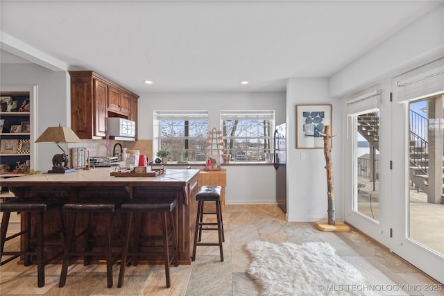 kitchen featuring tile countertops, white microwave, a peninsula, freestanding refrigerator, and a kitchen bar