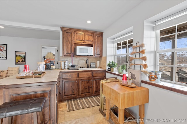 kitchen featuring tile counters, recessed lighting, decorative backsplash, white microwave, and a sink