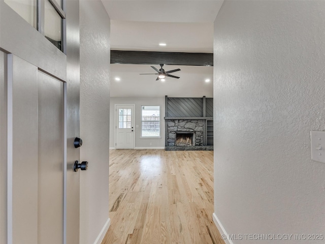 unfurnished living room featuring a stone fireplace, wood finished floors, beam ceiling, and baseboards