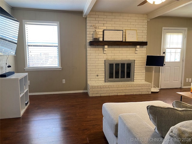 living area featuring a brick fireplace, plenty of natural light, dark wood-style floors, and beam ceiling