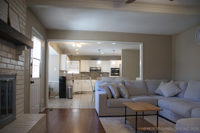 living room with a brick fireplace, a ceiling fan, and light wood-style floors