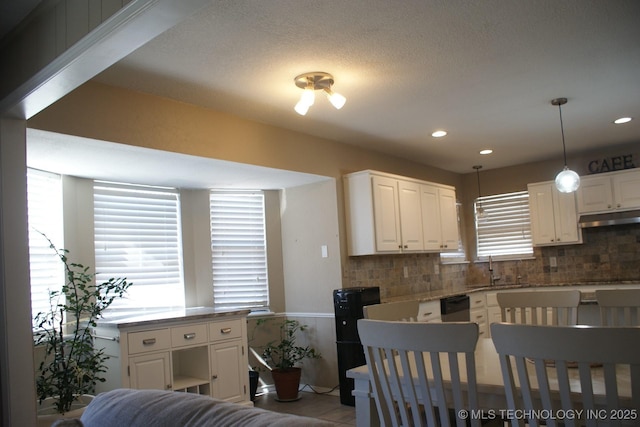 kitchen featuring white cabinets, a sink, under cabinet range hood, and decorative backsplash