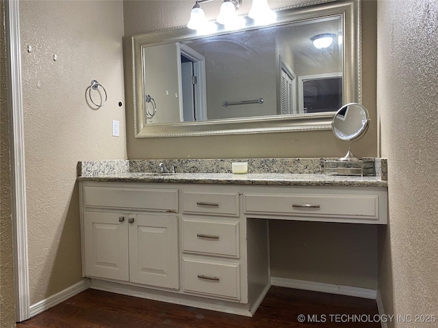 bathroom featuring a textured wall, vanity, baseboards, and wood finished floors