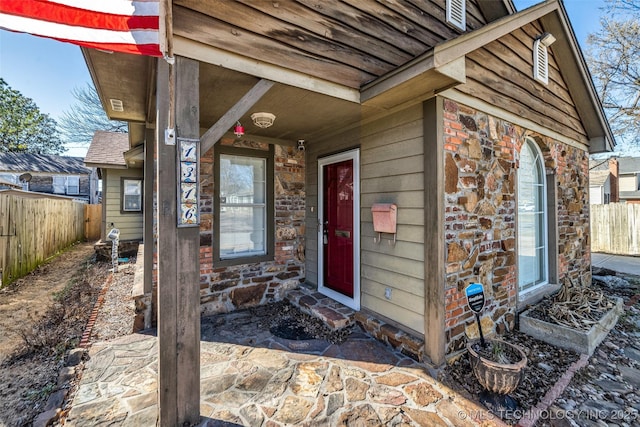 view of exterior entry with stone siding and fence