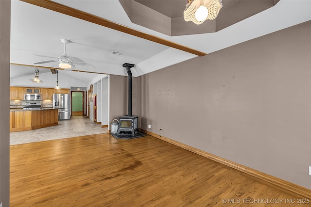 unfurnished living room with visible vents, ceiling fan, a wood stove, vaulted ceiling, and light wood-type flooring