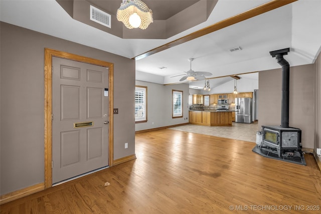 interior space with a wood stove, light wood-style flooring, visible vents, and baseboards