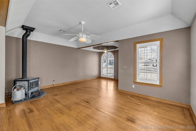 unfurnished living room featuring light wood finished floors, baseboards, visible vents, a ceiling fan, and a wood stove