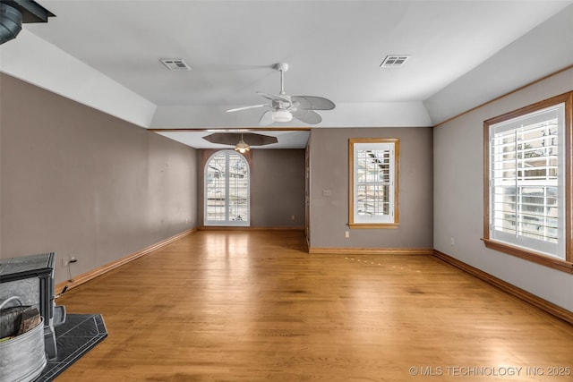 living room with visible vents, baseboards, a wood stove, and light wood-style floors