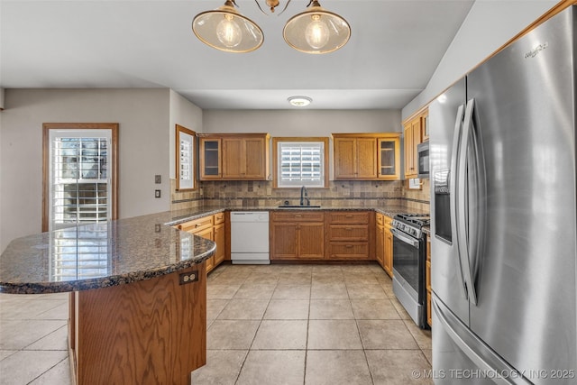 kitchen featuring brown cabinets, light tile patterned floors, appliances with stainless steel finishes, a sink, and a peninsula