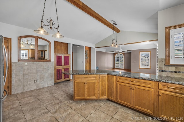 kitchen featuring brown cabinetry, dark stone counters, freestanding refrigerator, vaulted ceiling with beams, and pendant lighting