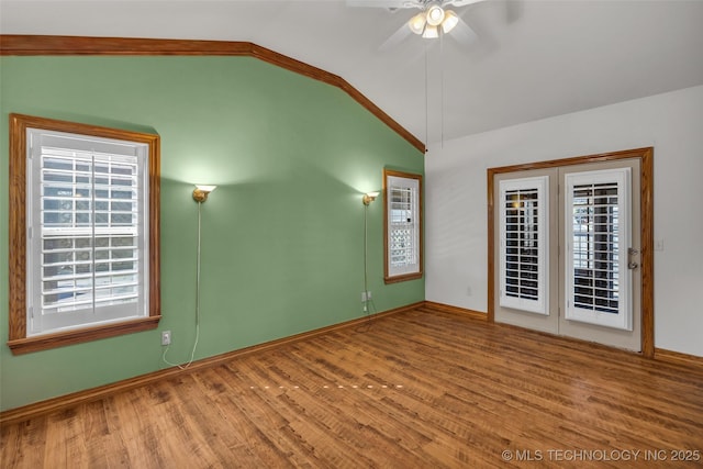 empty room with wood finished floors, a ceiling fan, baseboards, vaulted ceiling, and ornamental molding