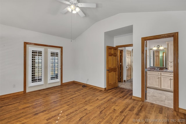 unfurnished bedroom with lofted ceiling, ensuite bathroom, a ceiling fan, baseboards, and light wood-style floors