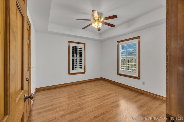 unfurnished bedroom with a tray ceiling, light wood-style flooring, and baseboards