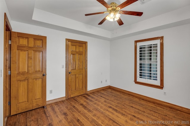 unfurnished bedroom with a tray ceiling, baseboards, and wood finished floors