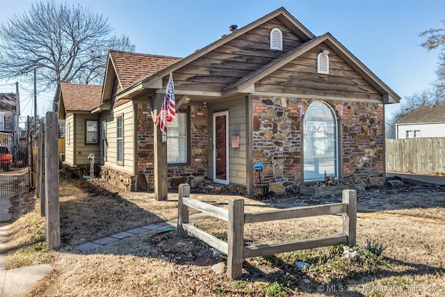 view of front facade with stone siding, a shingled roof, and fence