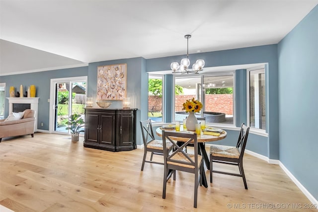 dining space with light wood-style floors, a fireplace, baseboards, and an inviting chandelier