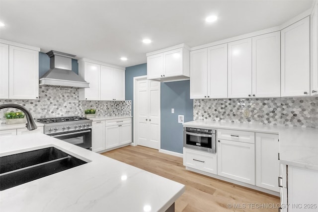 kitchen with stainless steel appliances, light wood-style floors, white cabinets, a sink, and wall chimney exhaust hood