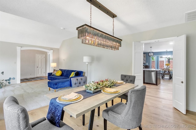 dining area featuring decorative columns, visible vents, light wood-style flooring, an inviting chandelier, and vaulted ceiling