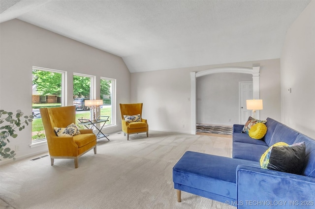 carpeted living area featuring arched walkways, visible vents, vaulted ceiling, a textured ceiling, and baseboards