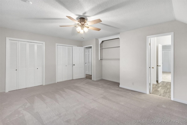 unfurnished bedroom with a textured ceiling, ceiling fan, carpet floors, baseboards, and two closets