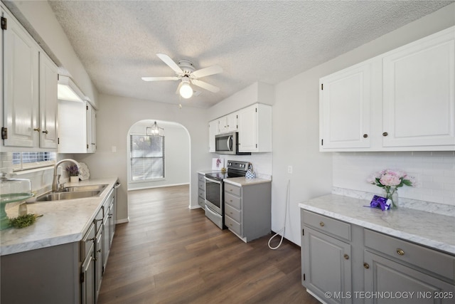 kitchen with arched walkways, a sink, gray cabinetry, dark wood-type flooring, and appliances with stainless steel finishes