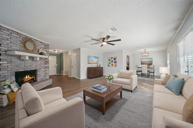 living room featuring wood finished floors, visible vents, ornamental molding, a textured ceiling, and a brick fireplace