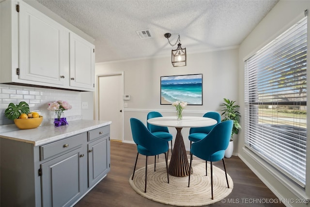 dining room featuring visible vents, a textured ceiling, dark wood-style floors, crown molding, and baseboards