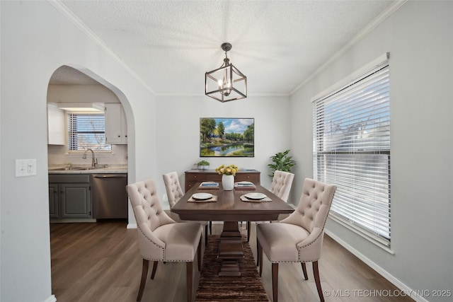 dining room with dark wood finished floors, a textured ceiling, arched walkways, and ornamental molding