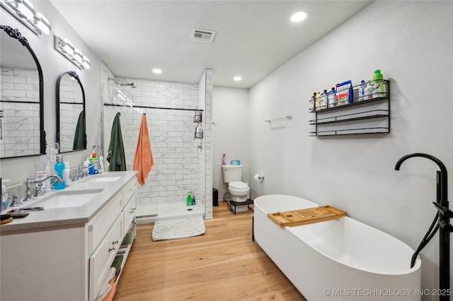 full bath featuring wood finished floors, a sink, visible vents, double vanity, and a stall shower