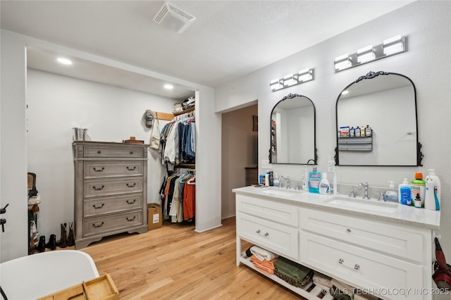 full bath with double vanity, visible vents, a sink, and wood finished floors