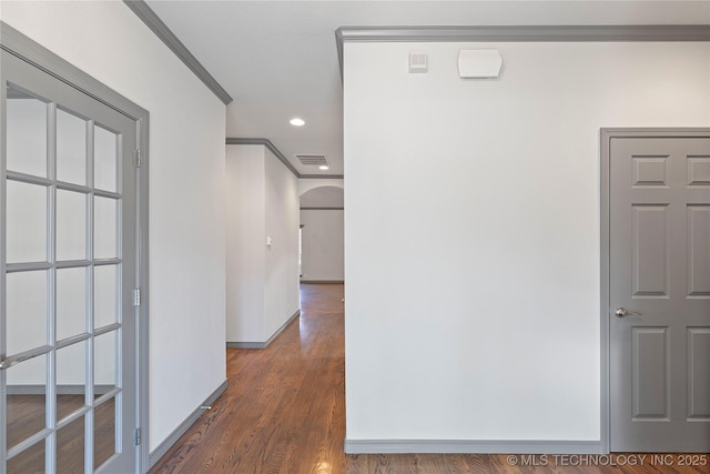 hall with baseboards, visible vents, arched walkways, dark wood-type flooring, and crown molding