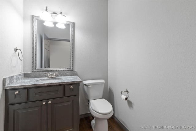 half bathroom with wood finished floors, vanity, toilet, and baseboards