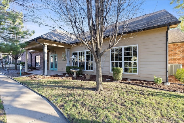 view of front of house with a shingled roof, brick siding, central AC, and a front lawn